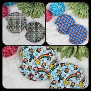 May include: Set of two round, colorful, fabric coasters featuring a checkered pattern with a rainbow, stars, and characters from the Super Mario Bros. video game.