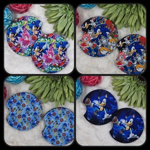 May include: Four sets of car coasters featuring the character Sonic the Hedgehog. Each coaster set has a different design, including Sonic with other characters, a pattern of Sonic and rings, and Sonic with a blue lightning background. The coasters are round with a curved notch.