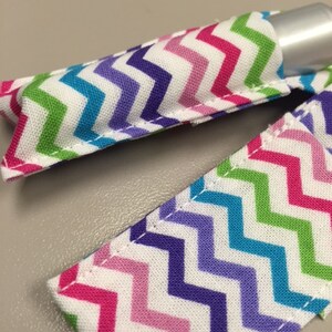 May include: A close-up of a colorful chevron patterned fabric pouch for a lip balm or small tube. The pouch is made of white fabric with pink, purple, blue, and green chevron stripes.