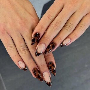 May include: Almond-shaped nails featuring a French manicure style with a brown and black tortoiseshell pattern on the tips. The nail design includes small, clear, round rhinestones placed along the transition line between the nude base and the dark pattern.
