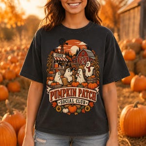 Peut inclure: Un t-shirt gris anthracite avec une impression graphique représentant quatre fantômes dans un champ de citrouilles. Le motif inclut une grange rouge, un moulin à vent et le texte PUMPKIN PATCH SOCIAL CLUB. Décoré de citrouilles et de feuilles.