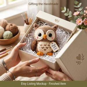 May include: A crocheted brown and cream owl toy with large black eyes and an orange beak, nestled in a white gift box filled with shredded paper. A small tag attached to the owl reads Made with Love. The box lid features a heart and leaf design.