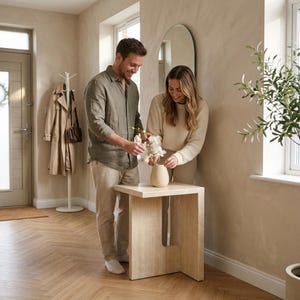 Può includere: Un tavolino in travertino beige chiaro con piano quadrato e base di supporto verticale caratterizzata da un'apertura rettangolare. Il tavolo è posizionato in una stanza con una parete chiara, un alto specchio ad arco e un appendiabiti.