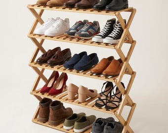 Puede incluir: Un zapatero plegable de madera de cinco niveles con acabado en marrón claro y un diseño de marco lateral en zigzag. Los estantes están llenos de varios estilos de calzado, incluyendo botas, zapatillas, mocasines, tacones y zapatos deportivos.