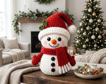 Puede incluir: Una figura de muñeco de nieve tejida a ganchillo con un gorro de Papá Noel rojo y blanco, adornado con hojas de acebo verdes y bayas rojas. El muñeco tiene una nariz de zanahoria naranja, ojos de botón negros y una bufanda roja con botones.