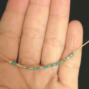 May include: A delicate necklace with a simple design featuring small turquoise and gold beads on a thin string.