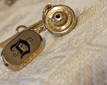 May include: Gold-toned tie tack with a black letter 'D' on a oval-shaped base and a round, textured back.