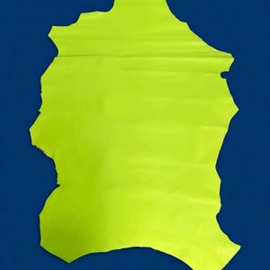 May include: A single, irregularly shaped piece of neon yellow leather with a smooth, matte surface. The hide features natural, jagged edges and a vibrant, high-visibility color that stands out against the dark blue background.