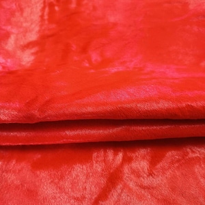 Könnte beinhalten: Ein leuchtend roter Stoff mit einer weichen, plüschigen Textur und einem dezenten Glanz. Das Material ist horizontal gefaltet, wodurch ein deutlicher Schichteffekt entsteht, der den dichten, kurzen Flor und die gleichmäßige, satte rote Farbe betont.