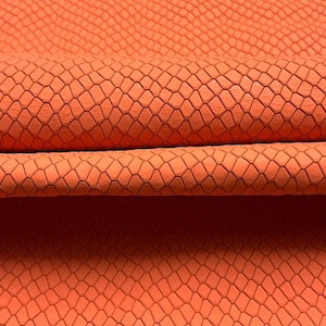 May include: A vibrant orange material featuring a repeating, embossed geometric pattern that resembles a textured scale design. The surface is folded, creating a horizontal ridge that highlights the depth and consistent pattern of the material.