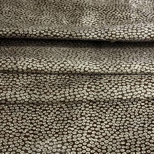 Könnte beinhalten: Ein dunkelbrauner Stoff mit einem sich wiederholenden Muster aus kleinen, cremeweißen, ovalen Markierungen. Das Textil ist in horizontalen Schichten gefaltet, was weiche Schatten erzeugt und die strukturierte Oberfläche des Materials hervorhebt.