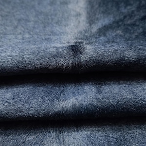Könnte beinhalten: Ein dunkelblaues, kurzhaariges Tierfell mit einer natürlichen, dichten Textur. Die Oberfläche weist subtile Variationen in Farbtiefe und Ton auf, wobei sichtbare Falten weiche Schatten auf dem Material erzeugen und die feine Maserung betonen.