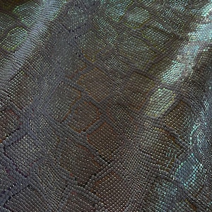 May include: A sheet of textured material featuring a repeating snakeskin pattern with an iridescent finish that shifts between dark charcoal, deep blue, and metallic green tones across the surface of the small, raised, scale-like geometric shapes.