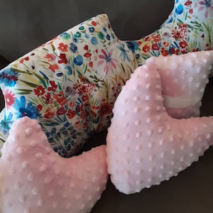 May include: Two pink heart-shaped pillows with a textured surface and a floral patterned pillow behind them.