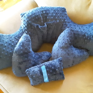 May include: A collection of blue, textured pillows in various shapes and sizes. The pillows have a soft, dotted surface and are arranged on a beige sofa. One small pillow has a blue ribbon.