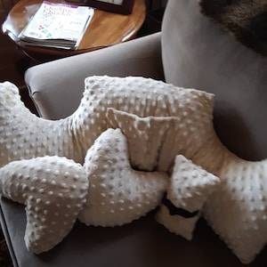 May include: A close-up of a beige couch with four white pillows with a textured surface. The pillows are arranged in a decorative pattern.