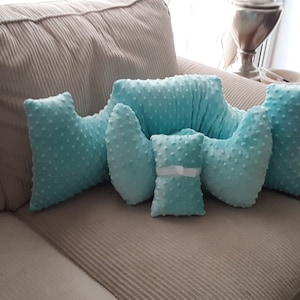 May include: A set of five light blue, plush pillows with a dotted texture. The pillows are arranged on a beige couch. The pillows are shaped like a crescent moon, a circle, and a rectangle.