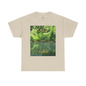May include: A beige short-sleeve t-shirt featuring a rectangular graphic print of a lush green forest reflected in a calm body of water. The text Rise is printed in gold above the trees, Return in the center, and Reflect below the water.