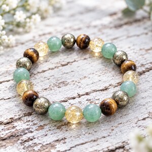 May include: A beaded bracelet featuring a repeating pattern of round polished gemstones. The beads include translucent light green aventurine, golden yellow crackle quartz, metallic pyrite, and brown tiger eye stones arranged in a circular loop.