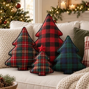 May include: A collection of four Christmas tree-shaped throw pillows in various fabric patterns. One features a large red and black buffalo check, while the others display red, green, and blue plaid designs. The smallest tree is topped with a red star.