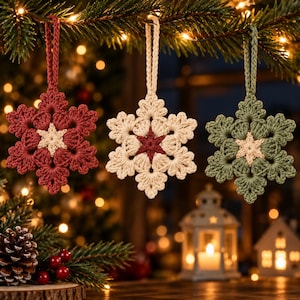 May include: Three crocheted snowflake ornaments hanging from a pine branch. The left ornament is dark red with a cream center, the middle is cream with a dark red center, and the right is sage green with a cream center. Each has a matching loop.
