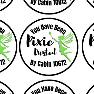 Könnte beinhalten: Ein Bogen mit zwölf runden Aufklebern, jeweils mit schwarzem Rand und dem Text "You Have Been Pixie Dusted By Cabin 10612" in schwarzer Schrift. Eine grüne Silhouette einer Fee mit Flügeln und Zauberstab ist rechts abgebildet.