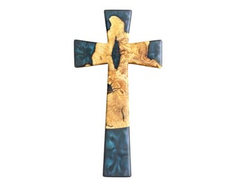 May include: A wooden cross with a unique design. The cross features a combination of light brown wood and dark teal resin. The wood grain is visible, adding texture. The cross is a religious symbol.