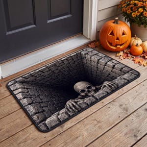 May include: A rectangular doormat featuring a 3D optical illusion of a deep, dark stone well. A realistic human skull and skeletal hands are depicted as if emerging from the edge of the well, rendered in shades of gray and black.