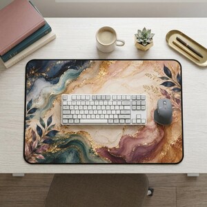 May include: A rectangular desk mat featuring a marbled pattern in shades of navy blue, deep red, and cream, accented with gold leaf details and dark botanical leaf illustrations. A white mechanical keyboard and a gray computer mouse sit on top.