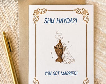 May include: A white greeting card with a gold filigree border, featuring a brown incense burner with a white lace veil and smoke, with the blue text SHU HAYDA?! and YOU GOT MARRIED! printed on the front, accompanied by a gold pen and envelope.