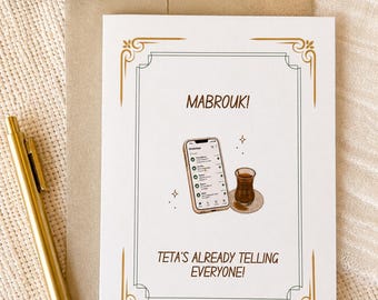 May include: A white greeting card with a gold decorative border featuring the text MABROUK! at the top and TETA'S ALREADY TELLING EVERYONE! at the bottom. The centre shows a smartphone displaying a WhatsApp chat list next to a small glass of tea.