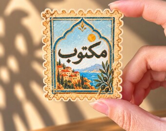 May include: A rectangular postage stamp sticker with scalloped edges featuring an illustration of a coastal Mediterranean village with orange-roofed buildings, a blue sea, and an olive branch. The Arabic word Maktoub is written in black script.