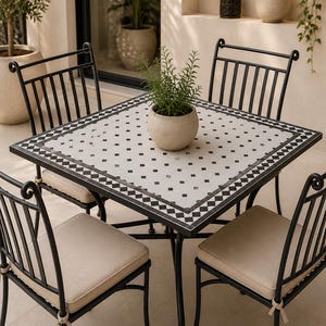 May include: A square dining table with a white and black checkered tile top and a black metal frame, accompanied by four matching black metal chairs featuring beige seat cushions. A small potted green plant sits in the centre of the table.