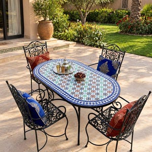 May include: An oval outdoor dining table with a blue, white, and brown mosaic tile top and a black metal frame, accompanied by four matching black metal chairs with scrollwork backs, each featuring a solid-coloured red or blue decorative pillow.
