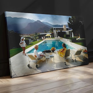 May include: A rectangular canvas print featuring a vibrant outdoor scene of a swimming pool surrounded by lounge chairs and people. The image displays a bright blue pool, green lawn, and distant mountains under a clear sky, capturing a sunny day.