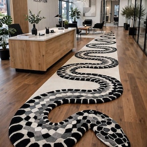 Puede incluir: Una alfombra larga y estrecha con forma de serpiente sinuosa, que presenta un patrón repetitivo de escamas hexagonales negras, blancas y grises. La alfombra se extiende por el suelo de madera, con la cabeza de la serpiente en primer plano.