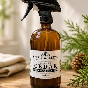 May include: An amber glass spray bottle with a black trigger nozzle. The white label reads Spirit Gardens Botanical Home + Garden Western Red Cedar All-Purpose Cleaner Steam Distilled Small Batch 16 FL OZ 473 mL with a dog and pinecone icon.