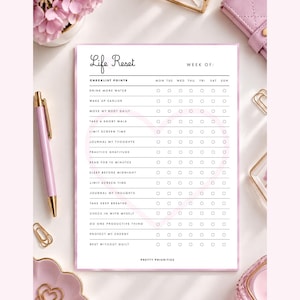 Peut inclure: Une feuille de suivi blanche intitulée Life Reset avec un contour de cœur rose pâle. Elle présente des lignes pour des habitudes quotidiennes comme boire de l'eau et lire, avec des colonnes pour chaque jour. Un stylo rose pâle est placé à gauche.