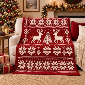 Könnte beinhalten: Eine rechteckige Strickdecke in tiefem Rot mit einem weißen Muster, das zwei Rentiere vor einem zentralen Tannenbaum zeigt, umgeben von horizontalen Bändern aus komplexen Schneeflockenmotiven und geometrischen Formen auf der gesamten Fläche.