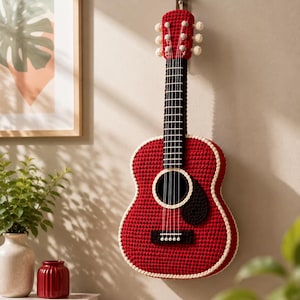 Peut inclure: Une guitare murale en crochet rouge avec une touche noire, une bordure blanche autour du corps et des chevilles d'accordage blanches. La guitare possède six cordes et un pickguard noir, avec une texture en laine imitant la forme d'une guitare.