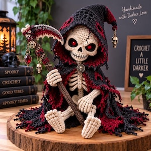 May include: A crocheted skeleton figure wearing a black and red hooded cloak with a tattered hem. The figure has glowing red eyes and holds a staff topped with a scythe, a pentagram charm, a red gem, and a small skull charm.