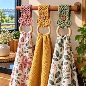 Peut inclure: Trois essuie-mains suspendus à une tringle en bois par des attaches crochetées rose poudré, jaune moutarde et vert sauge. Chaque attache comporte un bouton en bois et un anneau en bois clair retenant une serviette à motif floral ou gaufré.