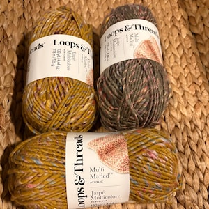 May include: Three skeins of Loops & Threads Multi Marled acrylic yarn. Two skeins are a mustard yellow with flecks of blue and pink, and one skein is a dark grey with multi-coloured flecks. Each label states 130 yd, 4.44 oz, and 126 g.