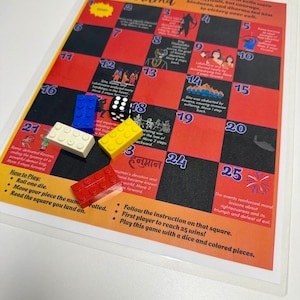 Könnte beinhalten: Ein Path of Dharma Brettspiel mit einem nummerierten Raster von 1 bis 25, das Illustrationen und Texte über Rama enthält. Das Spiel umfasst einen schwarzen sechsseitigen Würfel und vier Kunststoff-Bausteine in Rot, Blau, Gelb und Weiß.