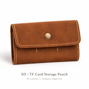 May include: A brown PU leather storage pouch for SD and TF cards featuring a rectangular shape, a fold-over flap with a single metallic snap button closure, and visible light-colored stitching along the edges. Text reads: SD / TF Card Storage Pouch PU Leather • Compact Organizer.