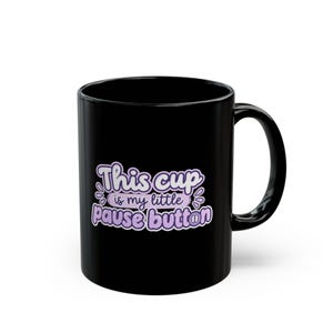 May include: A black ceramic mug featuring the text "This cup is my little pause button" in a light purple font with a white outline. The letter "o" in the word "button" is replaced by a pause symbol consisting of two vertical white lines.