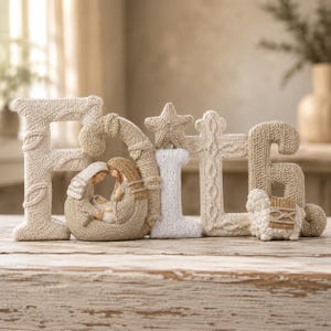 May include: A decorative tabletop sign spelling the word FAITH in a textured, knit-like finish. The letter A incorporates a nativity scene with figures in beige and white, while the letter I is topped with a star and the letter H features a lamb.