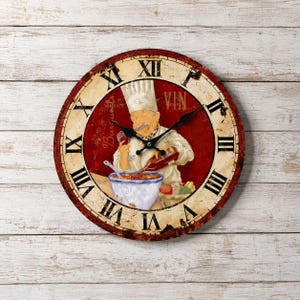 Puede incluir: Un reloj de pared redondo con esfera de color crema y rojo desgastado con números romanos negros. La ilustración central muestra a un chef con gorro blanco vertiendo vino tinto en un cuenco. El texto VIN aparece en el cuadrante superior derecho.