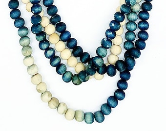 May include: A multi-strand necklace featuring round beads in alternating shades of dark blue and cream. The beads are arranged in several cascading loops, creating a layered effect with a consistent spherical shape throughout the entire piece.