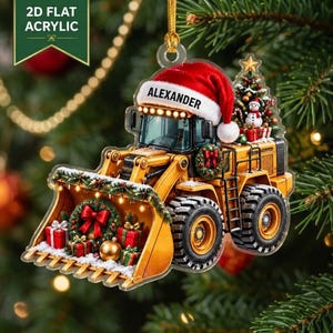 May include: A 2D flat acrylic Christmas ornament shaped like a yellow construction loader wearing a red Santa hat with the name ALEXANDER printed on the brim. The loader bucket is decorated with a green wreath, red bows, and wrapped gift boxes.